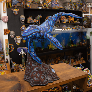 Escultura de ballena jorobada color azul sobre base color cafe cubierta con chaquiras
